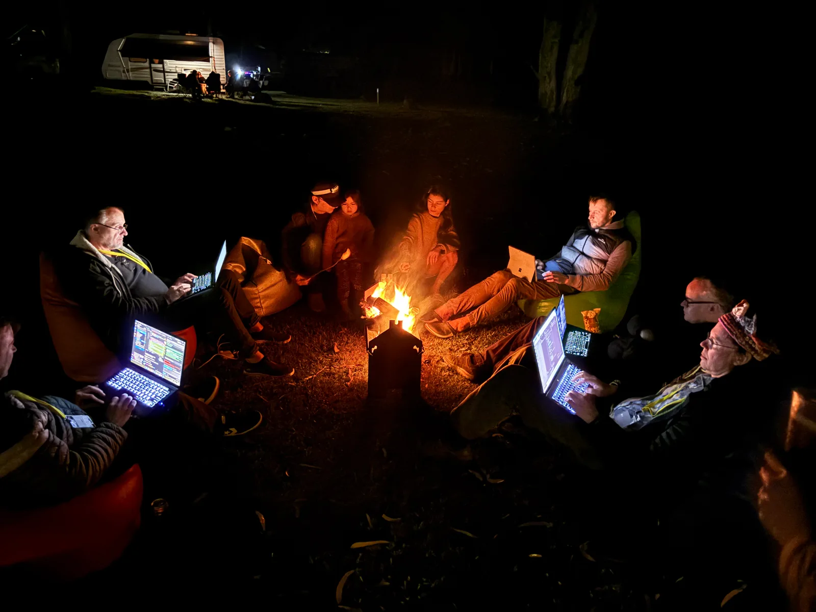 Hackers sitting around a campfire with laptops open at Vibecamp
